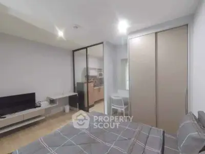 Modern bedroom with sleek design, featuring a cozy bed, TV, and a glimpse of a stylish kitchen.