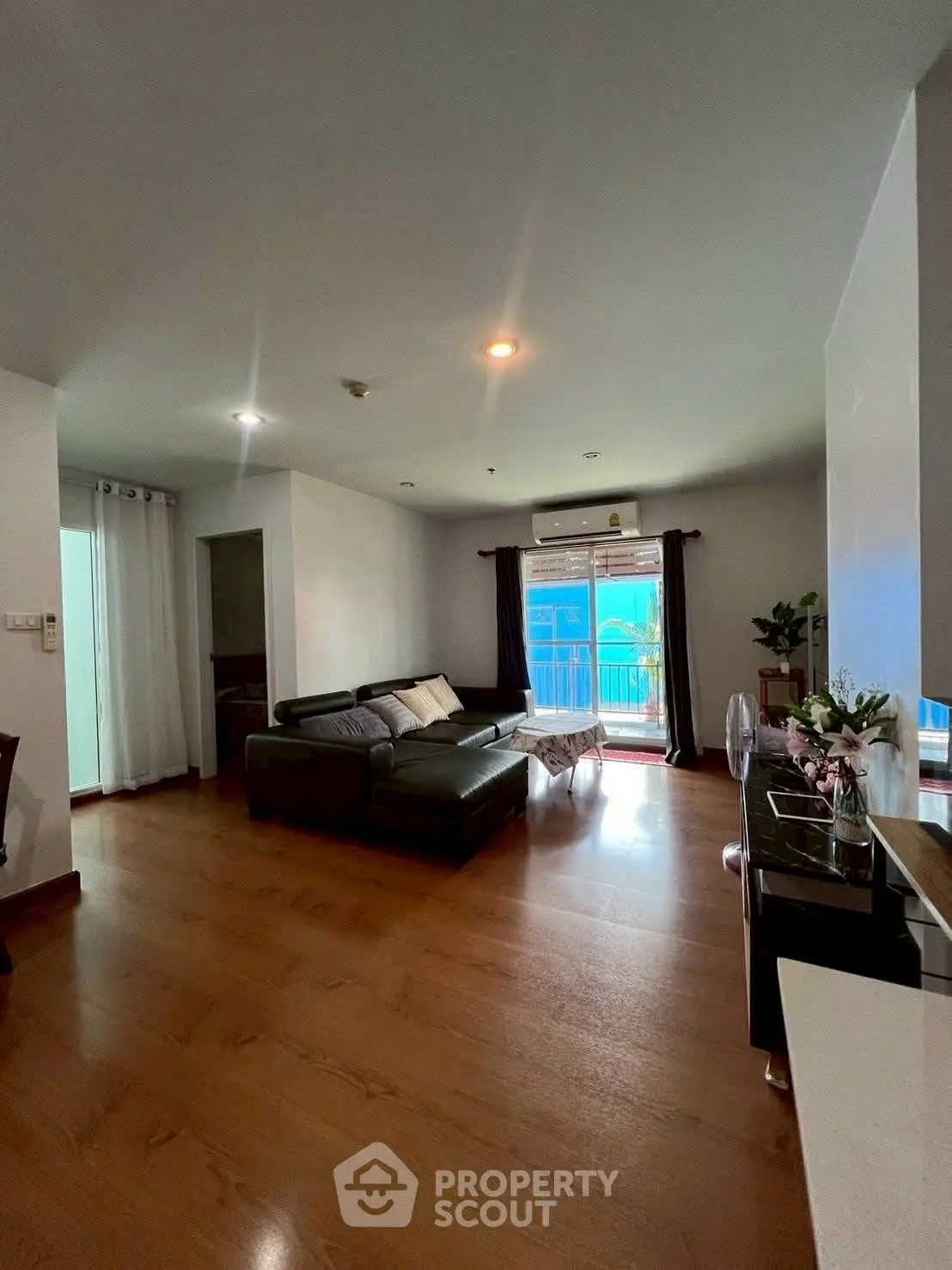 Spacious living room with wooden flooring and modern decor, featuring a large window for natural light.