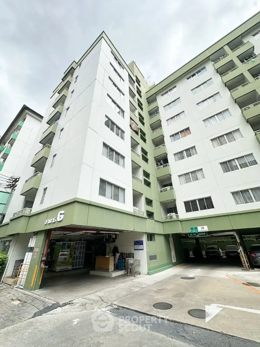 Modern multi-story apartment building with green accents and parking area, showcasing urban living.