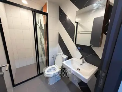 Modern bathroom with sleek design featuring a glass shower, stylish sink, and geometric wall tiles.