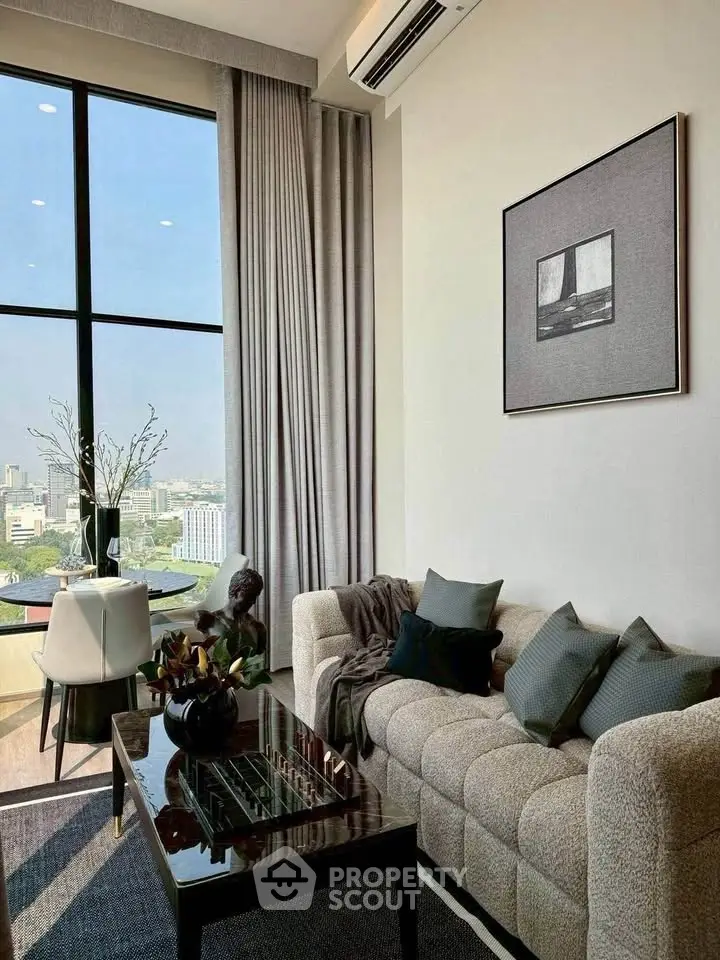 Stylish living room with large window offering stunning city views, elegant decor, and cozy seating.