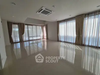 Spacious sunlit living room with large windows and elegant curtains