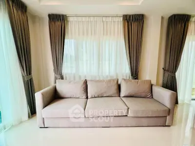Elegant living room with modern beige sofa and floor-to-ceiling windows with stylish curtains.