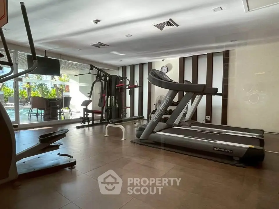 Modern gym with treadmills and exercise equipment in a bright, spacious room with pool view.