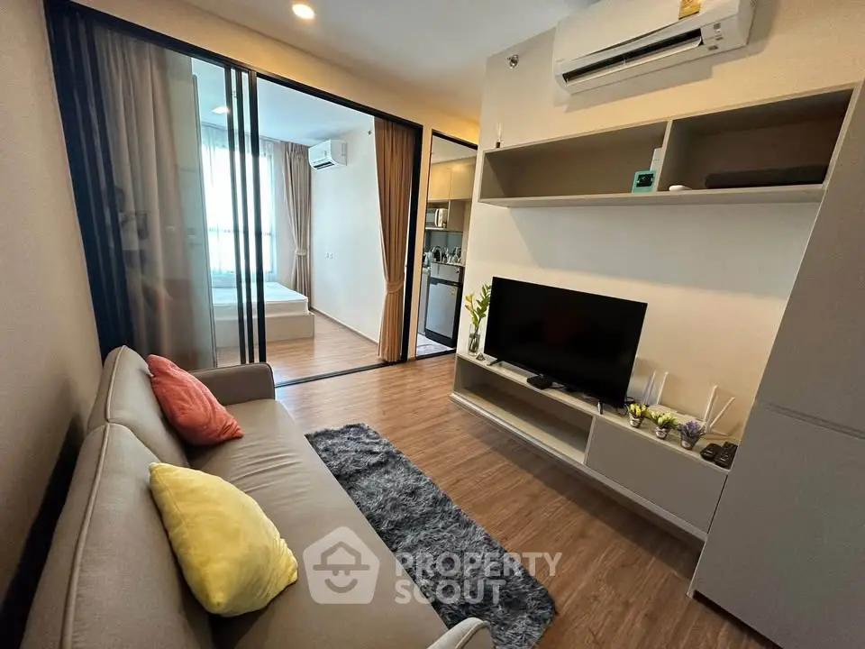 Modern living room with cozy sofa, TV, and open view to bedroom, featuring sleek design and natural light.
