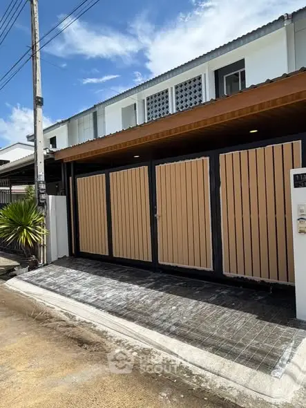 Modern townhouse exterior with wooden gate and driveway in sunny neighborhood.