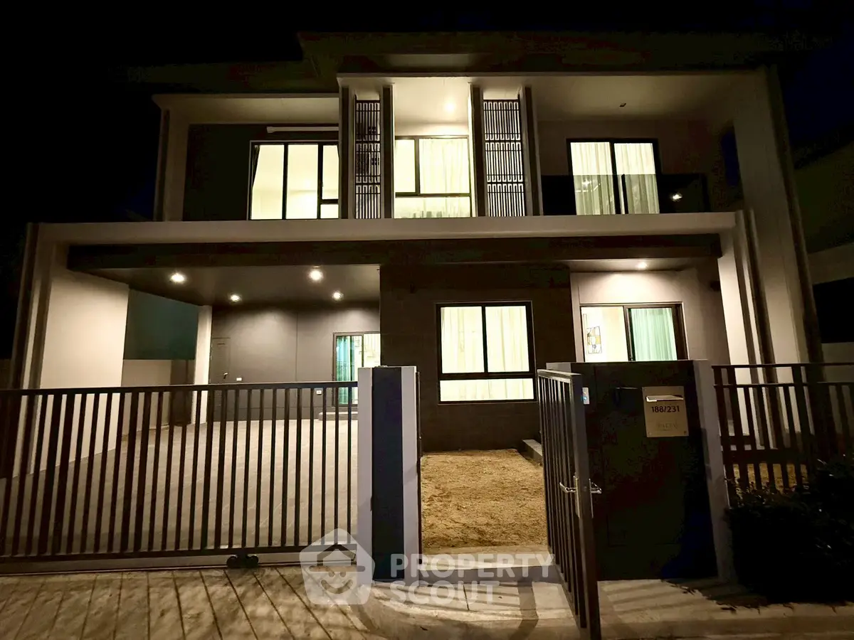 Modern two-story house with gated entrance and illuminated windows at night.