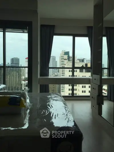 Modern bedroom with large windows offering stunning city views in a high-rise apartment.
