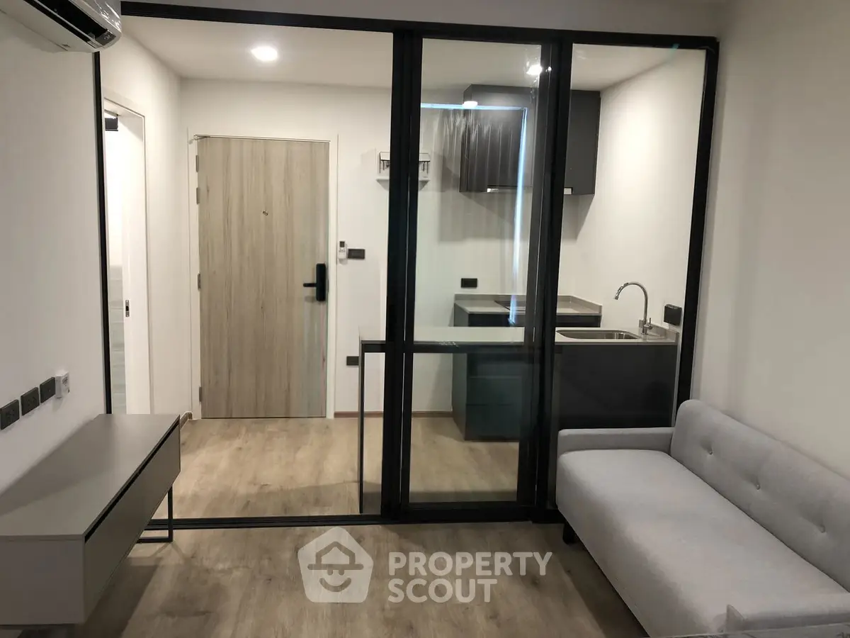 Modern studio apartment with sleek kitchen and cozy living area, featuring glass partition and stylish furnishings.