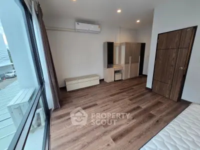 Spacious bedroom with modern wood flooring and large window for natural light.