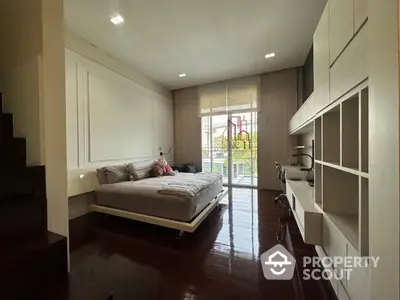 Spacious bedroom with glossy hardwood flooring, modern furnishings, and ample natural light streaming through large windows leading to a balcony.