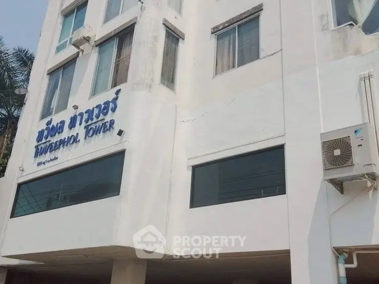 Exterior view of a white building with air conditioning unit and signage.