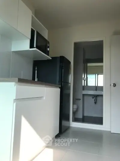 Modern compact kitchen with sleek appliances and adjacent bathroom in a bright apartment.