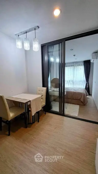 Modern apartment with glass partition separating dining area and bedroom, featuring elegant lighting.