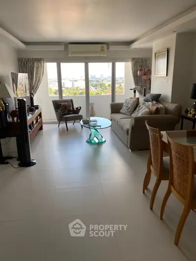 Spacious living room with large windows and city view, featuring elegant furniture and decor.
