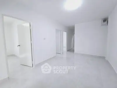 Spacious white-walled room with tiled flooring and multiple doorways, ideal for versatile interior design.