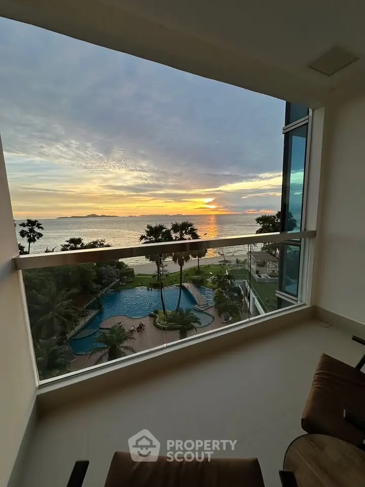 Stunning ocean view from a modern balcony overlooking a pool and lush greenery at sunset.