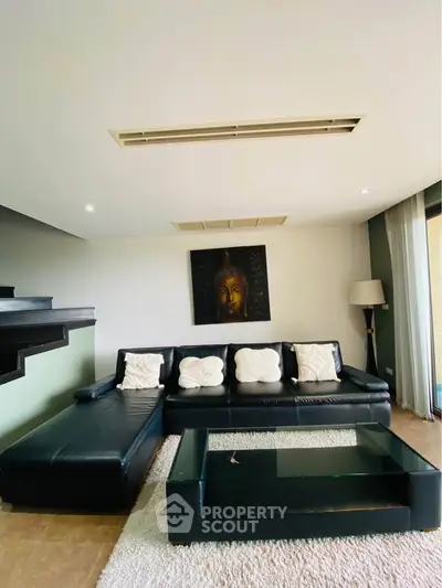 Spacious living room with modern black leather sofa and glass coffee table, featuring elegant decor and ambient lighting.