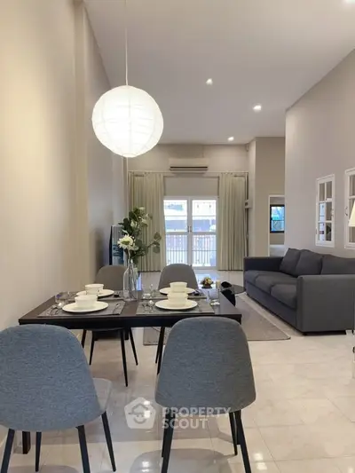 Modern living room with elegant dining area and stylish decor, featuring a cozy sofa and large windows.
