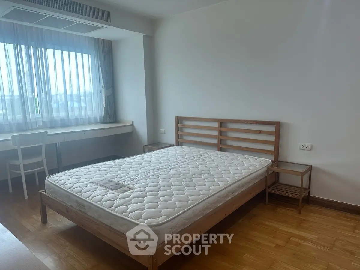 Spacious bedroom with wooden flooring and large window offering natural light.