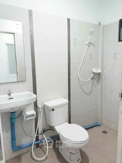 Modern bathroom with shower, toilet, and sink in a tiled setting.