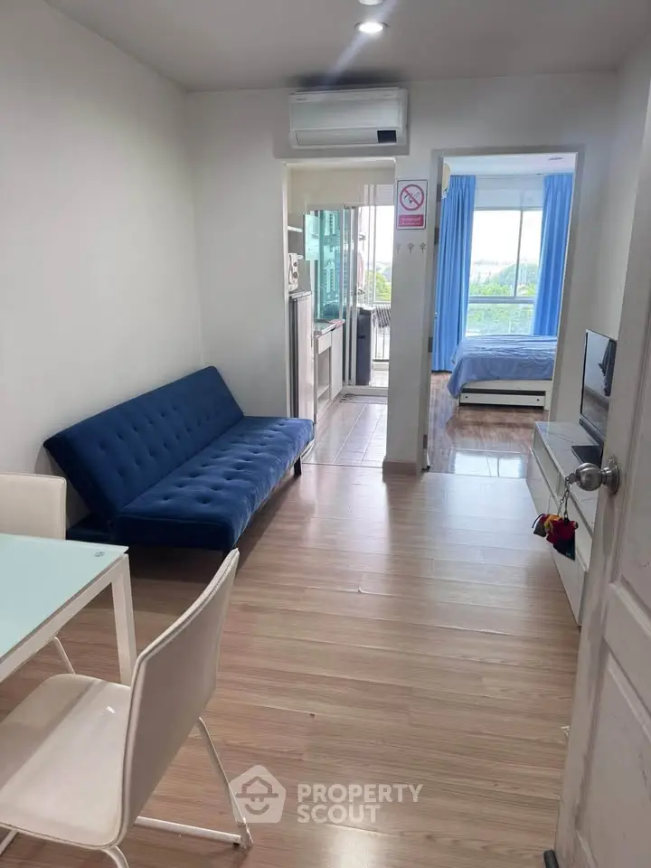 Modern apartment interior with open living room and bedroom view, featuring sleek furniture and natural light.