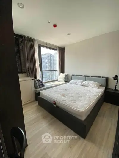 Modern bedroom with large window and city view, featuring a comfortable bed and stylish decor.