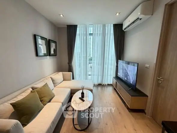 Modern living room with cozy sofa, large TV, and floor-to-ceiling windows offering city views.