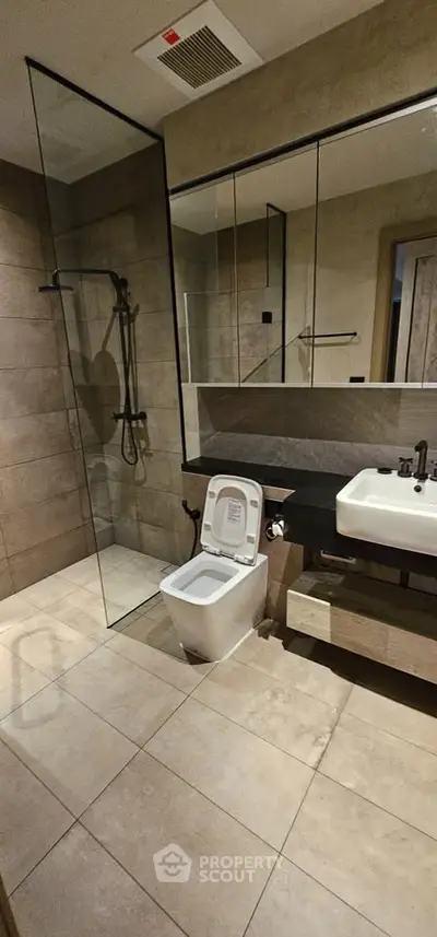 Modern bathroom with glass shower, sleek fixtures, and large mirror in contemporary apartment.