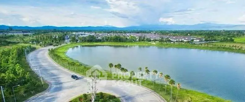 Scenic aerial view of a serene lake surrounded by lush greenery and distant mountains.