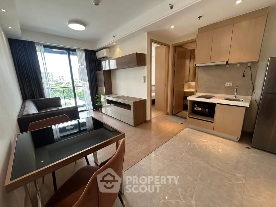 Modern open-plan living room with kitchen in a stylish apartment, featuring sleek furniture and city view balcony.
