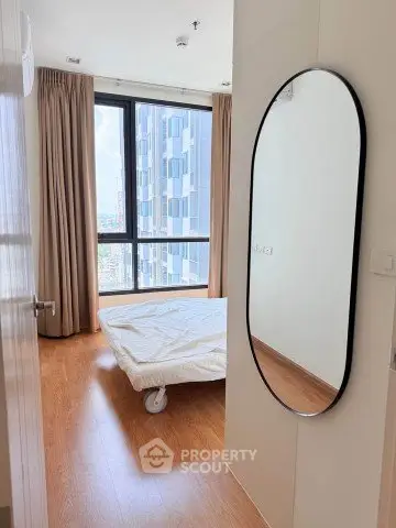 Modern bedroom with large window and stylish mirror in high-rise apartment.