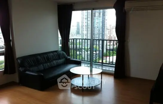 Modern living room with city view and sleek black sofa in high-rise apartment.