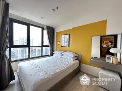 Bright and modern bedroom with large windows offering an urban view, accented by a bold yellow wall, creating a cozy yet vibrant living space.