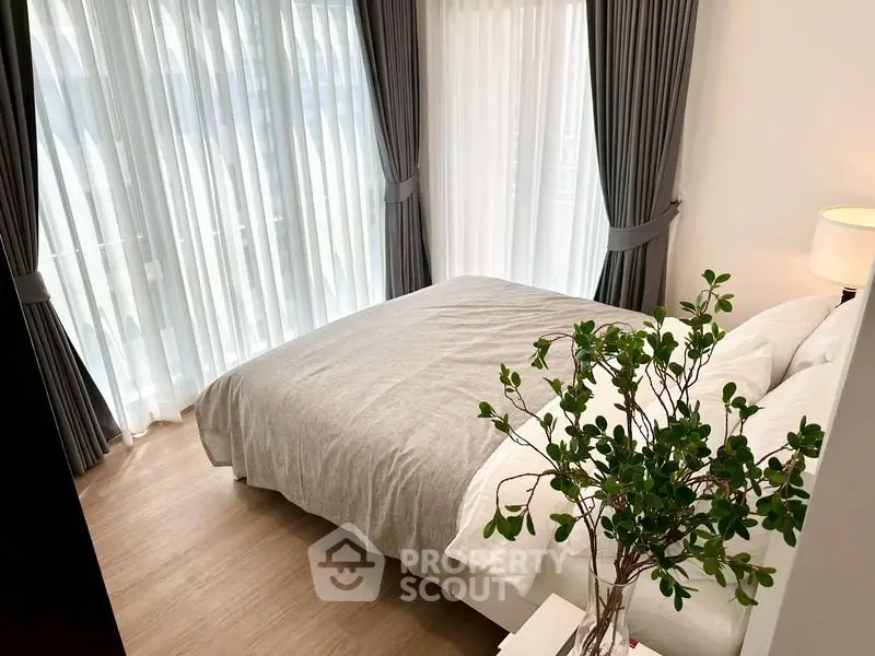 Cozy bedroom with large windows and elegant curtains, featuring a comfortable bed and stylish decor.