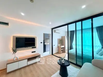 Modern living room with glass partition leading to a cozy bedroom, featuring sleek furniture and ambient lighting.