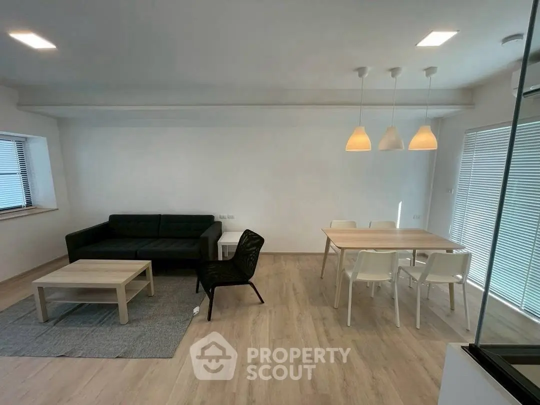 Modern living room with sleek furniture and dining area, featuring minimalist design and ample natural light.