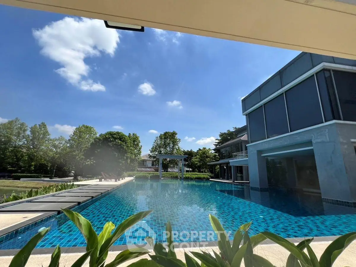 Luxurious modern poolside view with clear blue skies and lush greenery.