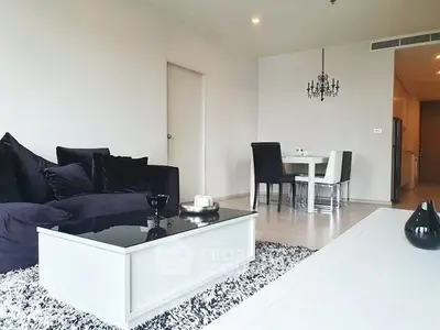 Modern living room with elegant decor and dining area, featuring plush seating and stylish chandelier.