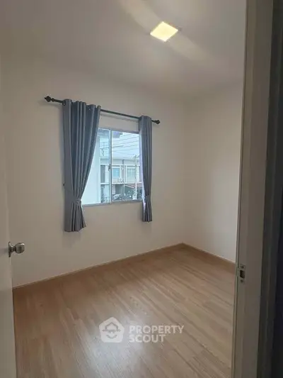 Bright empty room with wooden flooring and window view, ideal for customization.