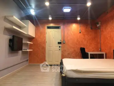 Modern studio apartment with vibrant orange accent wall and sleek furnishings.