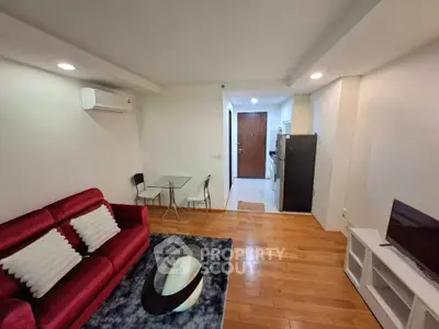 Modern living room with red sofa, wooden flooring, and compact dining area in open layout apartment.