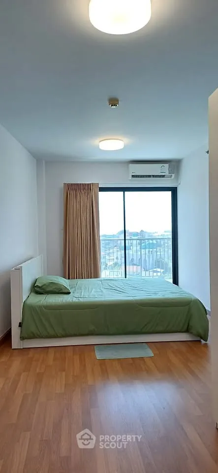 Spacious bedroom with balcony and city view, featuring wooden flooring and modern lighting.