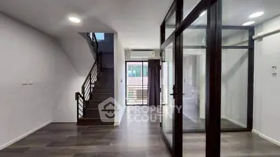 Modern duplex interior with glass partition and staircase, featuring sleek wooden flooring.