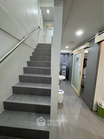 Modern interior with sleek staircase and laundry area, featuring a washing machine and minimalist design.
