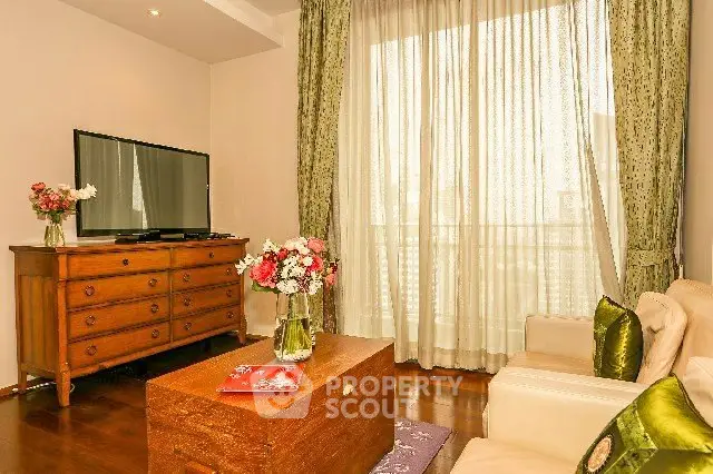 Charming living room with elegant decor, featuring a TV, wooden furniture, and large window with sheer curtains.
