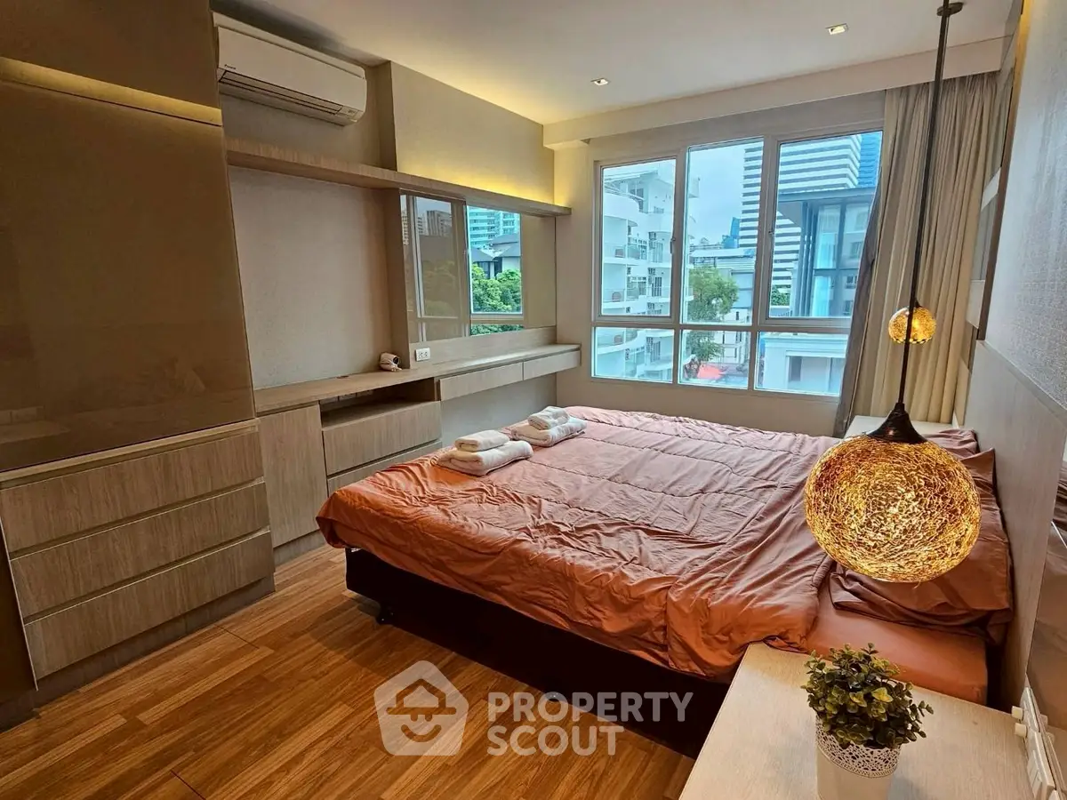 Modern bedroom with large windows and stylish lighting in urban apartment.