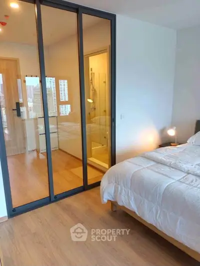 Modern bedroom with glass sliding doors and city view, featuring cozy bedding and wooden flooring.
