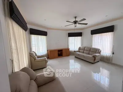 Spacious living room with elegant furniture and ceiling fan, featuring large windows and natural light.