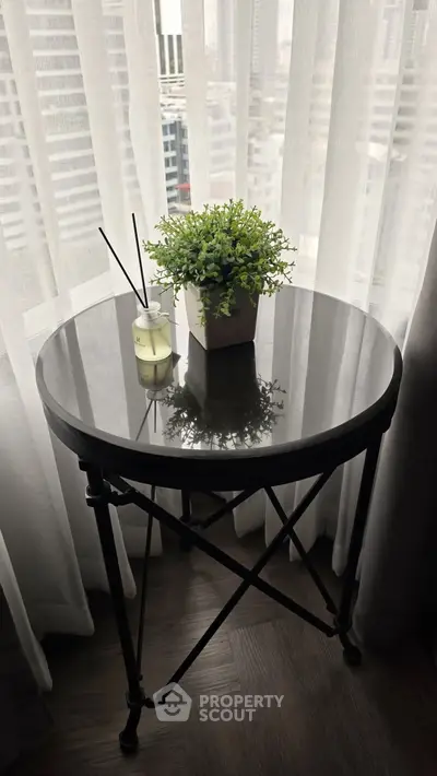 Stylish round table with plant and diffuser by window in modern apartment.